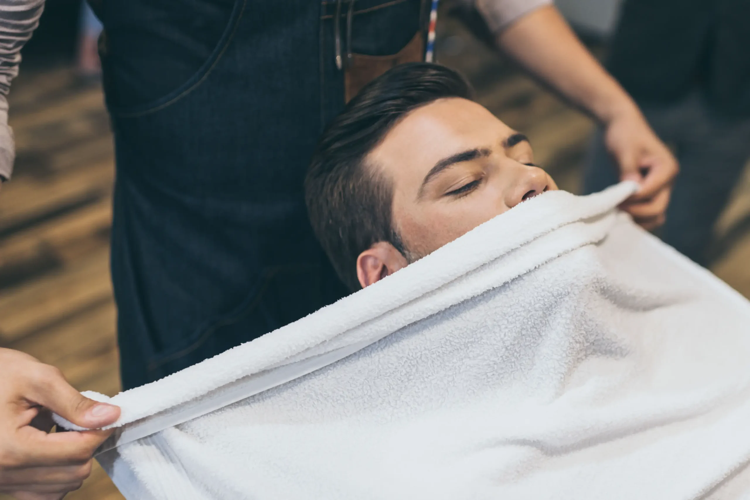 Barber applies a hot towel treatment to a male client before a shave.